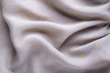 Soft folds of a light pink synthetic fabric texture with yellow gold ornaments to be used as...