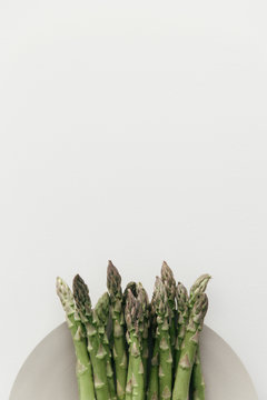 A plated batch of raw green asparagus on a white table.