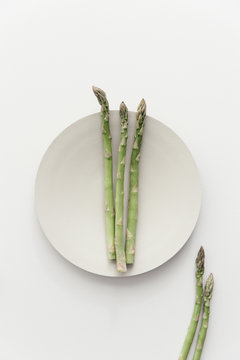 A plated batch of raw green asparagus on a white table.