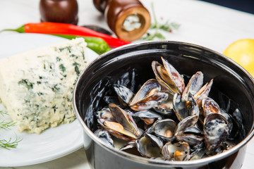 mussels in cheese sauce dor blu, in a black saucepan. On a white wooden background, decorated with vegetables and cheese.