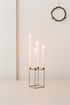 Four burning advent candles in a candle holder on the last Sunday before Christmas with a rosemary wreath in the background of a white interior.