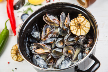 mussels in garlic sauce. in a black pan. On a white wooden background, the background is decorated with vegetables.