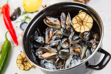 mussels in garlic sauce. in a black pan. On a white wooden background, the background is decorated with vegetables.