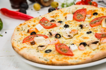 pizza with tomato, cheese and seafood on a white wooden background. Background decorated with vegetables.