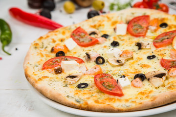 pizza with tomato, cheese and seafood on a white wooden background. Background decorated with vegetables.