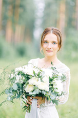 The bride in a wedding dress in nature with a bouquet. Boudoir photo shoot in pine lemu in the style of fine art.