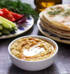 Vegan food, homemade hummus with flatbread, vegetables and olive oil on a concrete background.