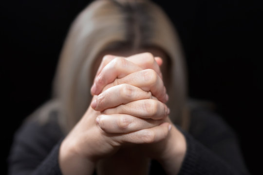 Woman praying with her hands clasped in front of her face, in dark room
