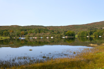 Boats moored at the southern end of Coniston Water on a tranquil early autumn morning in the Lake District, Cumbria, UK