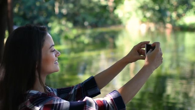 Pretty tourist girl with stunning smile taking photos with phone