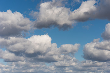 Beautiful white and grey fluffy clouds soar over a deep blue background. Cloudscape with autumn dark storm clouds moving fast over blue sky day.