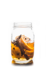Spicy mandarines beverage in jar with cloves, anise and cinnamon. Isolated on white. Selective focus. Shallow depth of field.