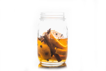 Spicy mandarines beverage in jar with cloves, anise and cinnamon. Isolated on white. Selective focus. Shallow depth of field.