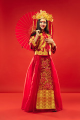 Chinese traditional graceful woman at studio over red background. Beautiful girl wearing national costume. Chinese New Year, elegance, grace, performer, performance, dance, actress, dress concept