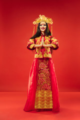 Obraz na płótnie Canvas Chinese traditional graceful woman at studio over red background. Beautiful girl wearing national costume. Chinese New Year, elegance, grace, performer, performance, dance, actress, dress concept