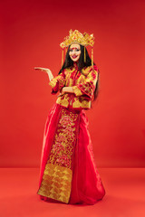 Chinese traditional graceful woman at studio over red background. Beautiful girl wearing national costume. Chinese New Year, elegance, grace, performer, performance, dance, actress, dress concept