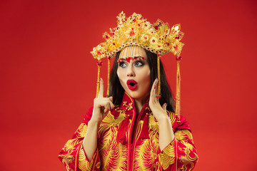 Chinese traditional graceful woman at studio over red background. Beautiful girl wearing national costume. Chinese New Year, elegance, grace, performer, performance, dance, actress, dress concept