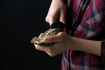 Woman opening raw oyster with knife against dark background
