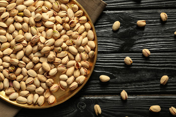 Metal tray with tasty pistachio nuts on wooden background
