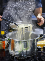 Chef takes out with slotted spoon hot steaming egg noodles from the pan