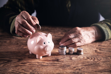 Elderly woman putting money to piggy bank.