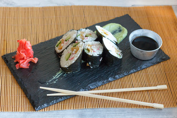 Japanese rolls with cucumber, crabs and omelet on a black board with wasabi and ginger