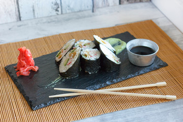 Japanese rolls with cucumber, crabs and omelet on a black board with wasabi and ginger