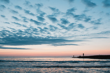Beautiful cloudy sunrise on Black Sea shore with fisherman on dock