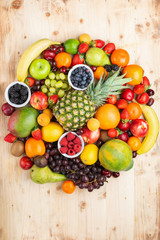 Circle filled with healthy colorful fruits, strawberries raspberries oranges plums apples kiwis grapes blueberries mango persimmon on light wooden table, top view, copy space for text, selective focus