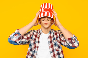 man in glasses is happy to watch a movie, with a bucket of popcorn on his head, on a yellow background