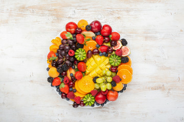 Healthy fruit platter, strawberries raspberries oranges plums apples kiwis grapes blueberries mango persimmon on the white wooden table, top view, copy space for text, selective focus