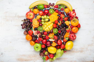 Heart made from healthy rainbow fruits platter, strawberries raspberries oranges plums apples kiwis grapes blueberries mango persimmon pineapple on wooden table, top view, copy space, selective focus