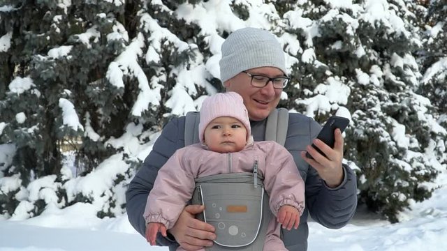 Young father with his baby in carrier with phone talking working father