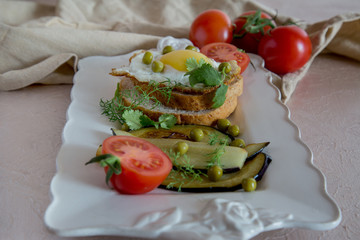 Dried egg on toast bread, eggplant, tomatoes and green peas as breakfast on white plate