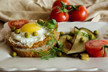 Fototapeta na wymiar Dried egg on toast bread, eggplant, tomatoes and green peas as breakfast on white plate