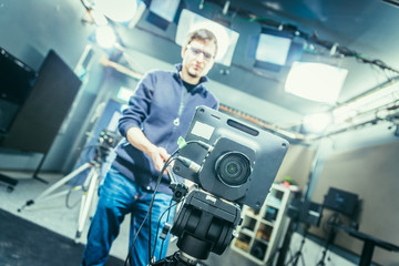 Fototapeta na wymiar Film camera in broadcasting studio, spotlights and equipment, cameraman in the blurry background