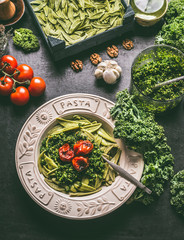 Homemade pasta with raw kale pesto and grilled tomatoes in plate with fork on kitchen table with...