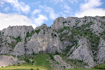 Sunny summer day, white clouds over mountain peak, where tourists climb to conquer fear, find courage and develop lateral thinking skills to overcome the difficulty of climbing a mountain. Small road 