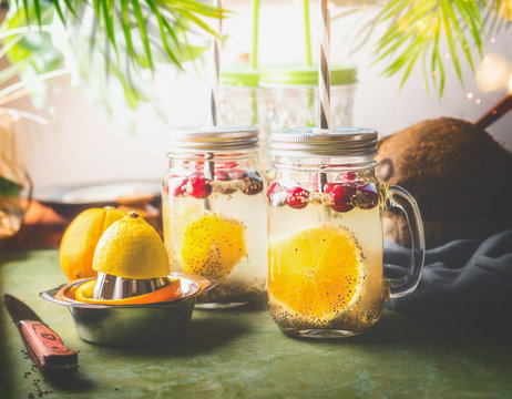 Detox chia seeds drink with orange fruit slice , lemon juice and cranberries in glass jars with drinking straw on kitchen table with ingredients. Summer drinks concept. Fitness and diet nutrition