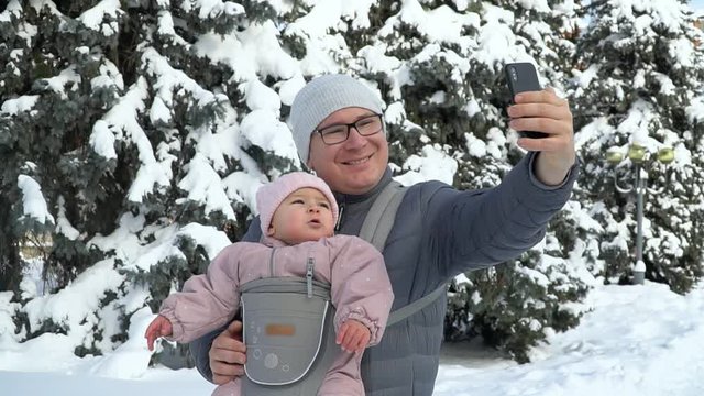 Young father with his baby in carrier with phone talking working father