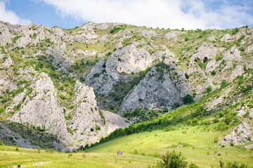Obraz premium Sunny summer day with white clouds over a mountain peak, where tourists climb to conquer fear, find courage and develop lateral thinking skills to overcome the difficulty of climbing a mountain. 