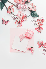 Pretty greeting card mock up in coral color with flowers, ribbon, little gift box and hearts on white background, top view. Flat lay. Abstract love and holidays concept. Blog layout. Pastel color