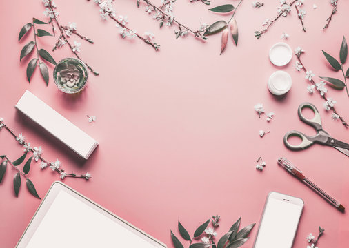 Smartphone and tablet pc mock up on pastel pink desktop background with modern cosmetics, stationery supples  and blossom branches, top view. Beauty blog and female business concept. Flat lay frame