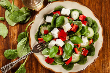 Fresh spinach salad with feta, cucumber and red paprika on a pla