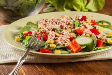 Fresh spinach salad with tuna, cucumber, corn, and red paprika on a plate