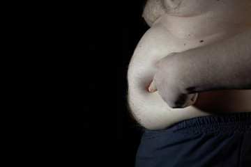 Unhealthy man checking his belly in front of dark background.