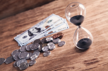 Hourglass and money on a wooden background.