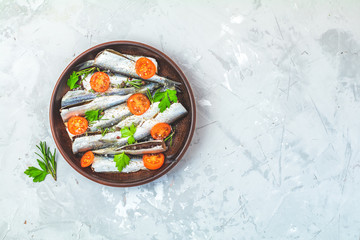 Sardines or baltic herring with rosemary, parsley, tomatoes slices and spaces on ceramic plate