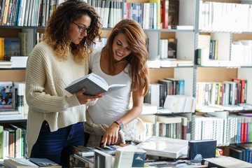 Two young woman in book store.They read and examining new bestseller.