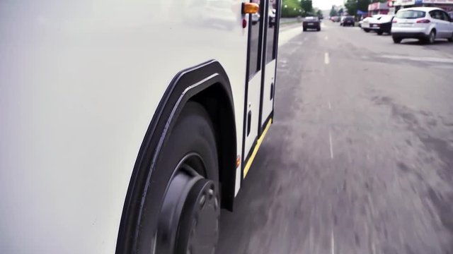 Close up view from the wheels and tires on the road of a bus riding around town. Scene. White bus moves down the street in the center of the city.